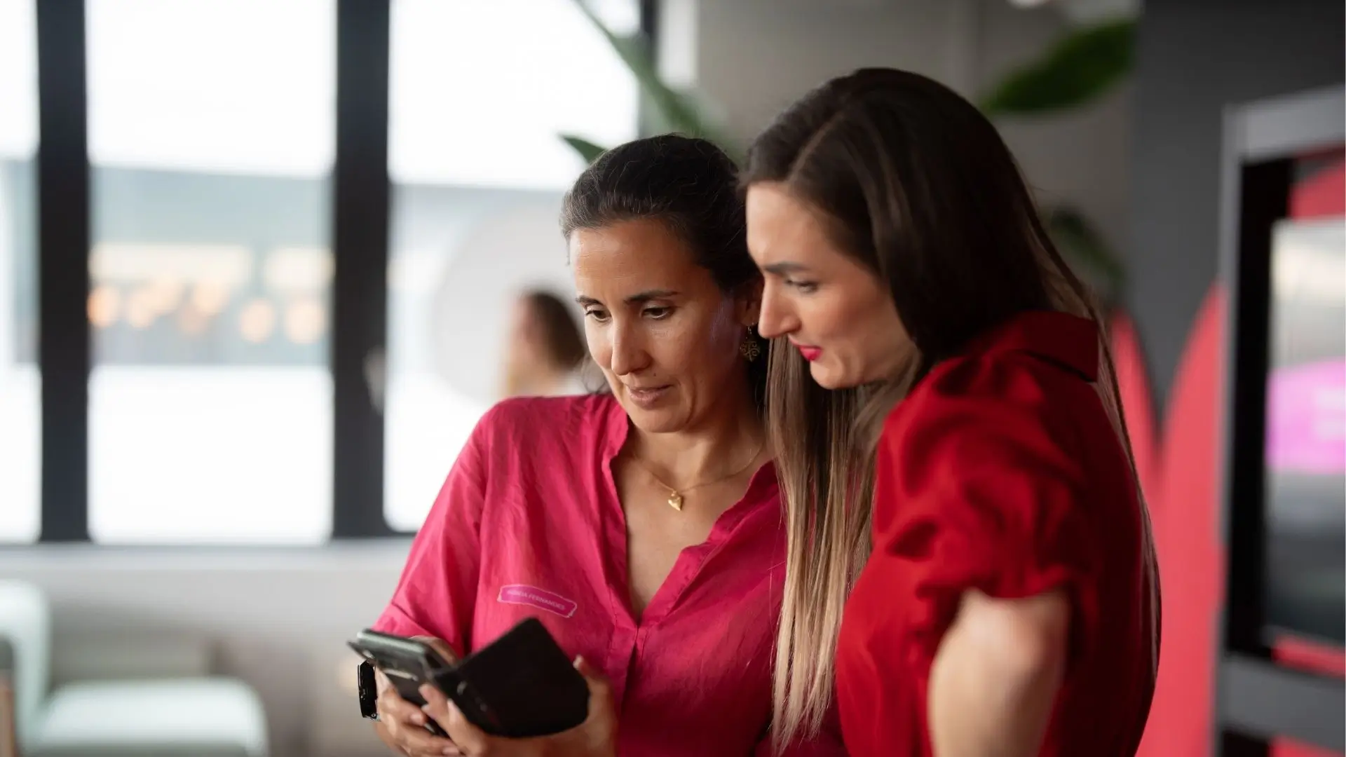 Andreia Fernandes (Founder of Portfolio Career PFC and SEABRAND Intl. GmbH) in a discussion about "How to start a passion-led portfolio career in 2026" with a peer woman. Both women wear red shirts, The setting is an female event in a modern office building