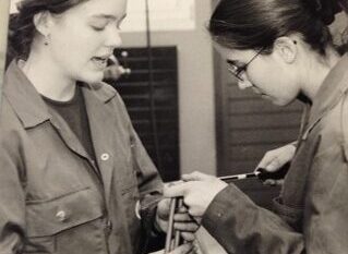 Schwarzweissfoto von zwei jungen Frauen in Arbeitskleidung bei einer technischen Werkstattarbeit oder einem praktischen Training.